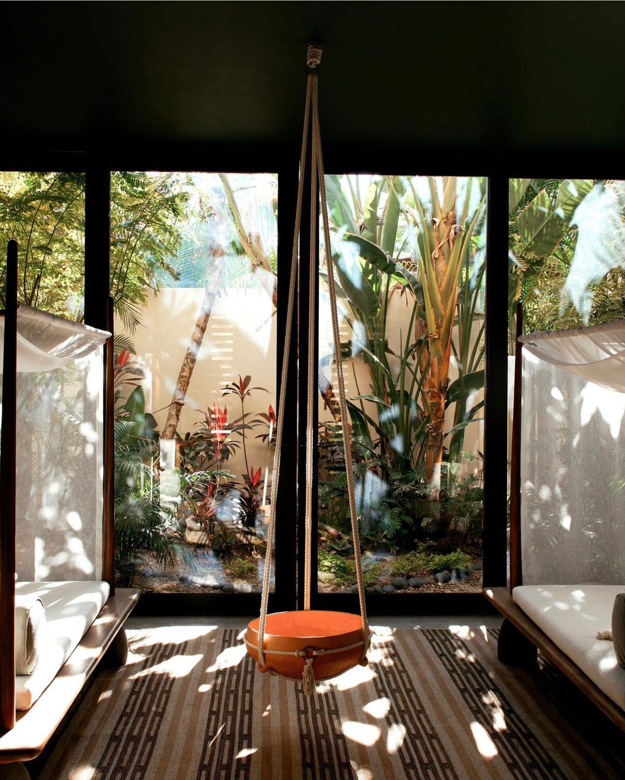A hanging swing chair in a glass room full of palms, by Studio DEA